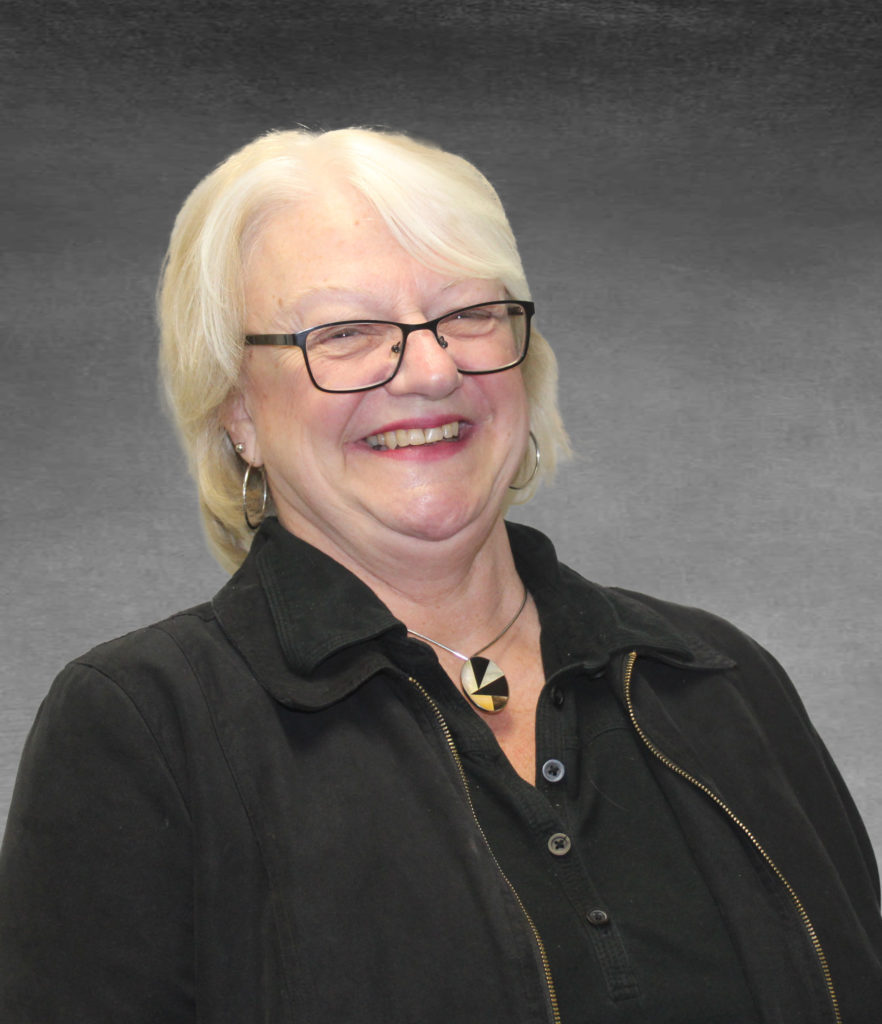 Professional headshot of Deb smiling. She is wearing a black button up top with a black jacket and a black and white pendant necklace