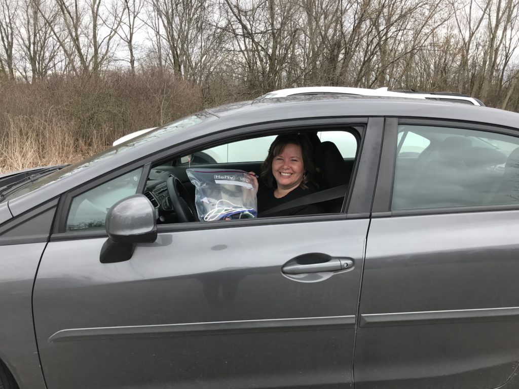 Woman in her car holding bag with face shield and mask