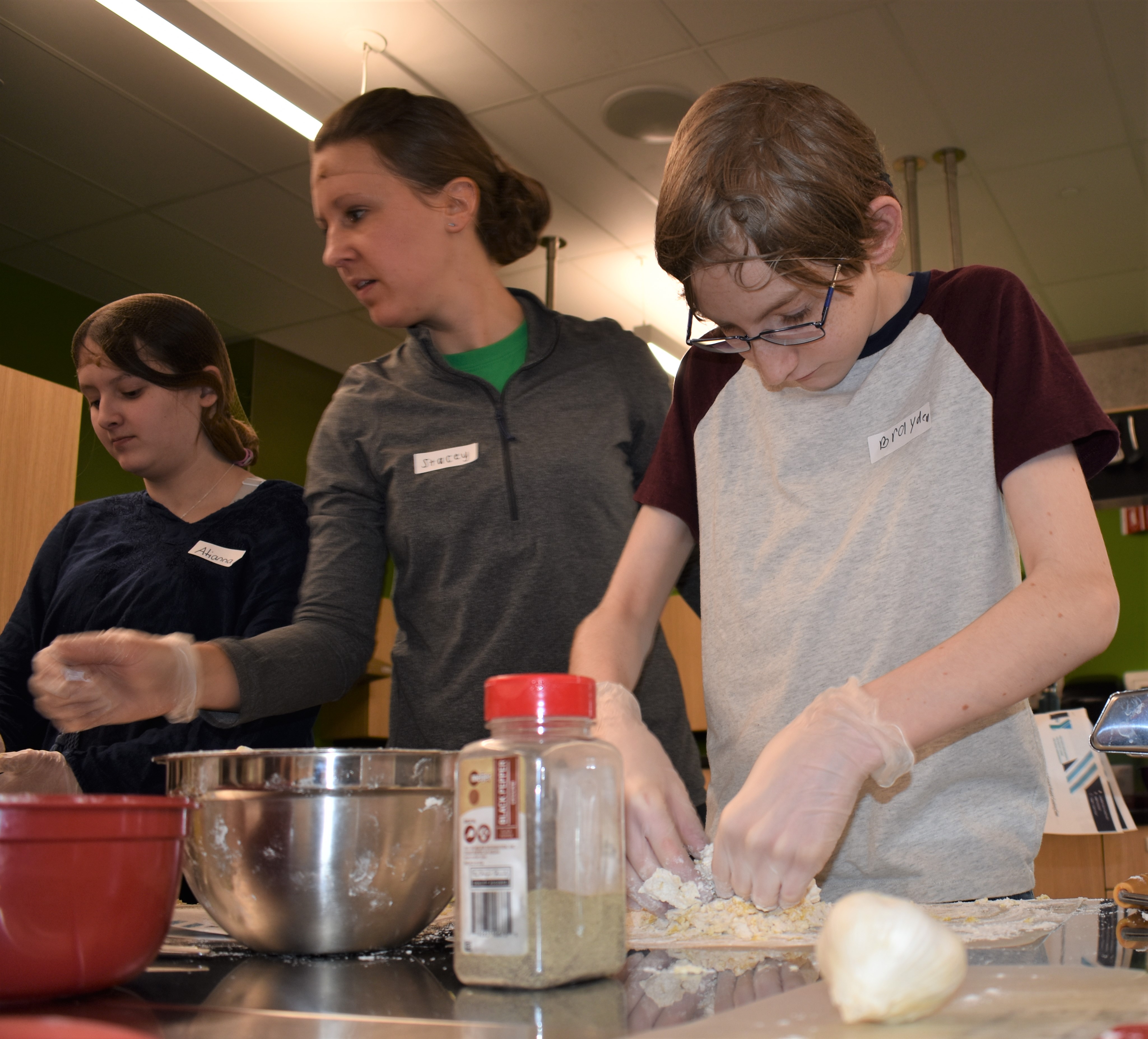 Image: Young boy cooking with ingredients in the foreground. Two women are in the background