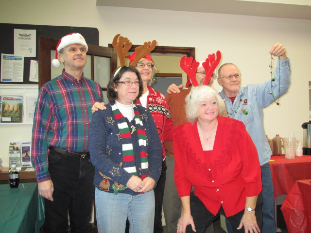A group of people at a holiday party. They are wearing holiday sweaters and reindeer antlers