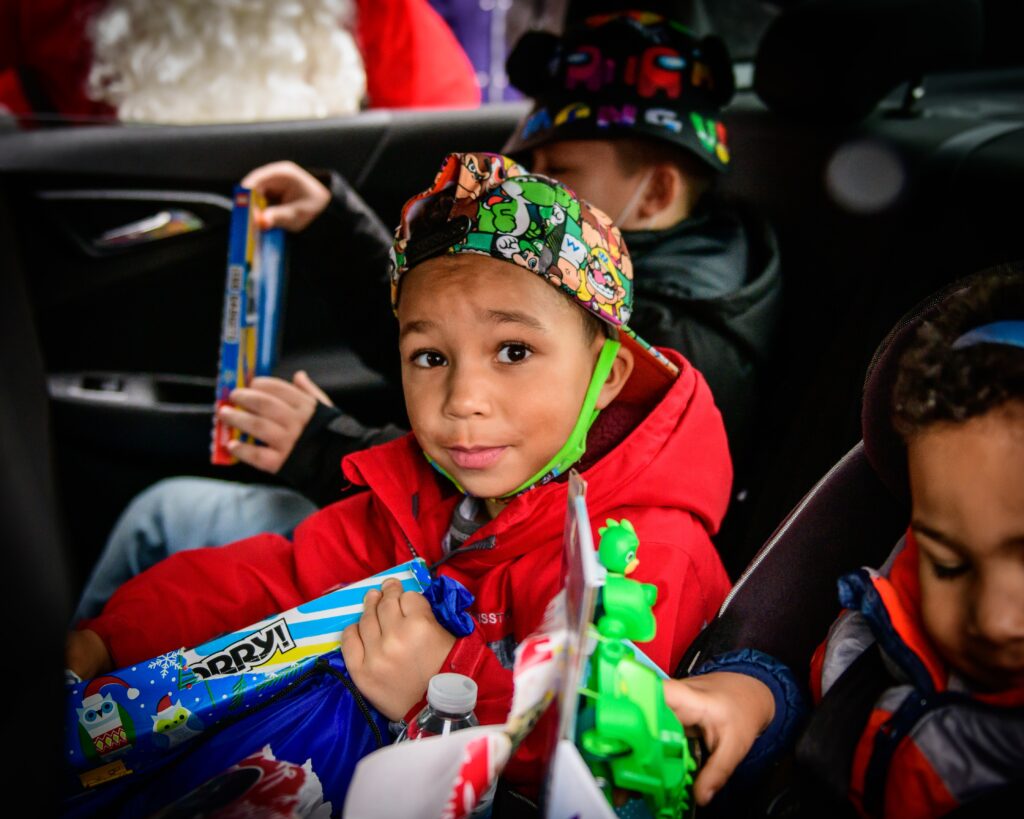 Three children in the backseat of a car opening gifts from santa