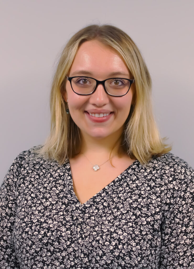Headshot of Erica. She is blonde with glasses and a black and white floral shirt.