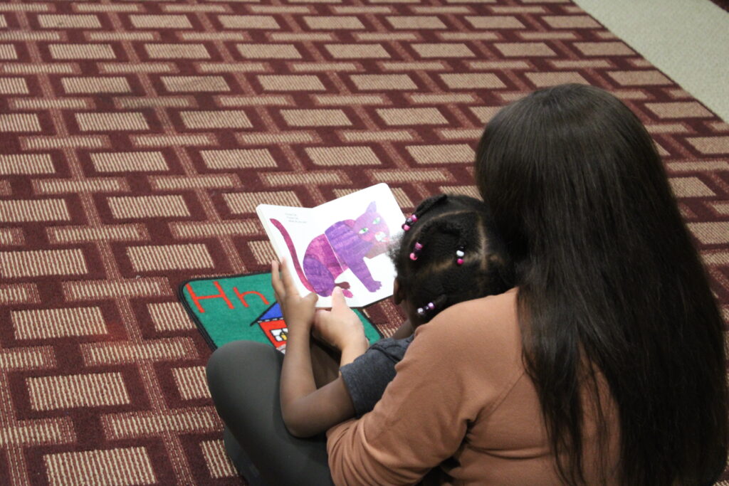 A young girl and and woman look at a book with a purple cat on it