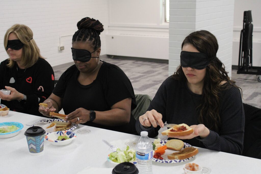 Three workshop attendees participate in the lunchtime activity. They are making sandwiches blindfolded