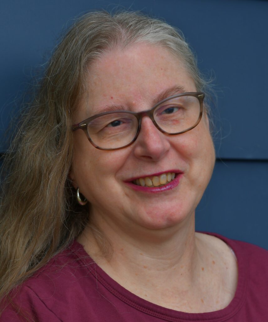 Headshot photo of Gail. .She is wearing dark framed glasses and a red shirt. She is in front of a blue background