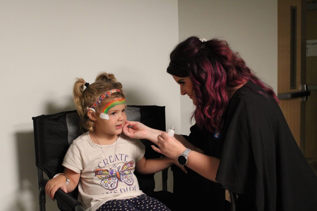A woman is painting a rainbow on a child's face
