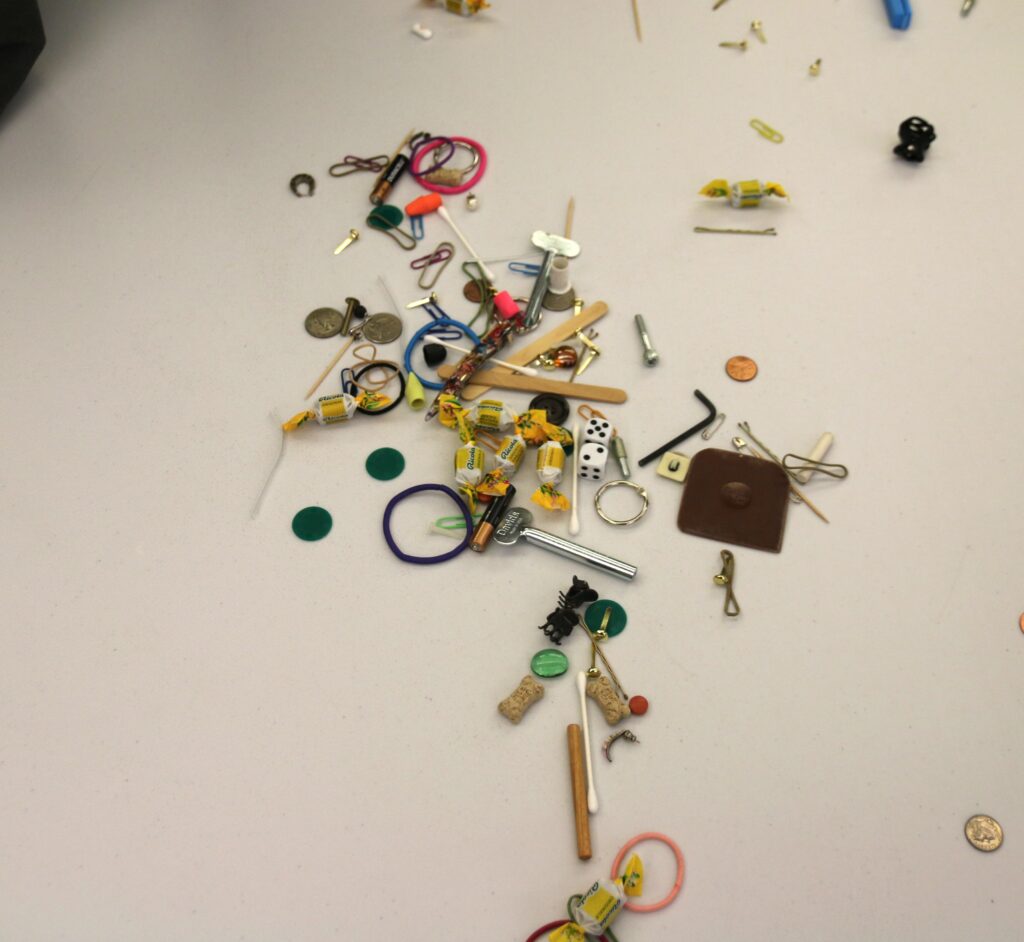 Various items scattered on a white table top, including buttons, coins, rubber bands, pins, and more