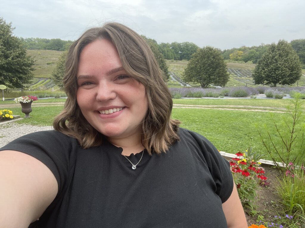 Photo of Haley smiling with grass and flowers in the background