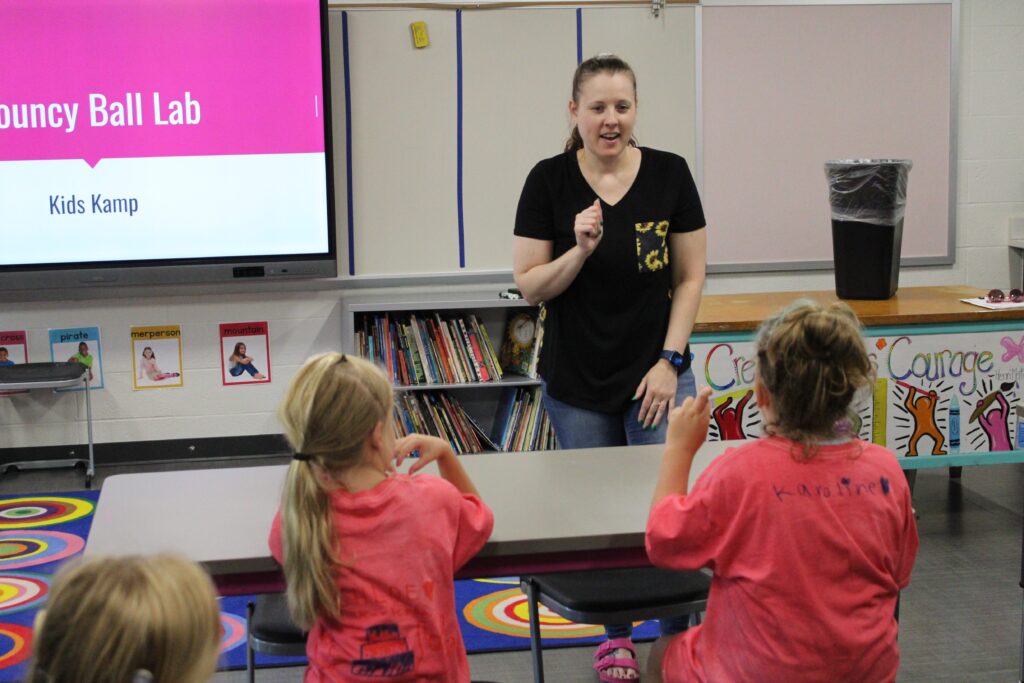 Woman standing at the front of a classroom and children sitting at tables