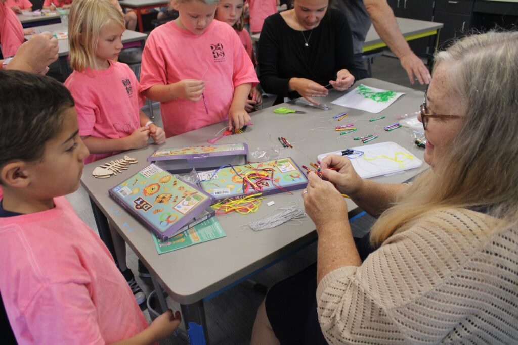 Kids gathered around a table doing an art activity. A woman is helping a boy in the foreground